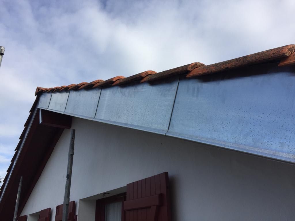 Bandeau de rive en zinc sur le pignon d'une maison à volets rouges